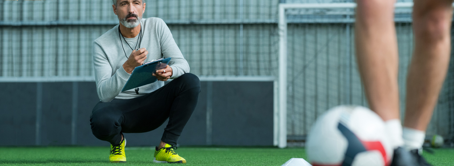 male coaching croached down looking at soccer players legs