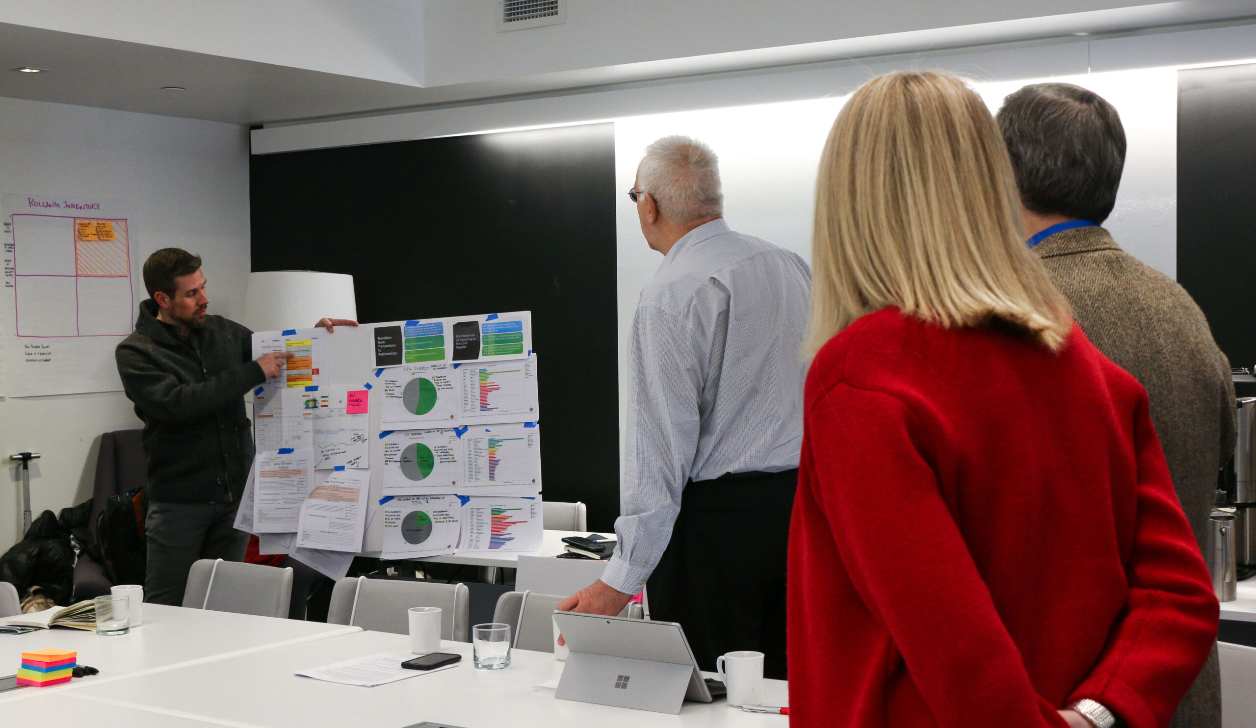 Man at board explaining with people around him listening