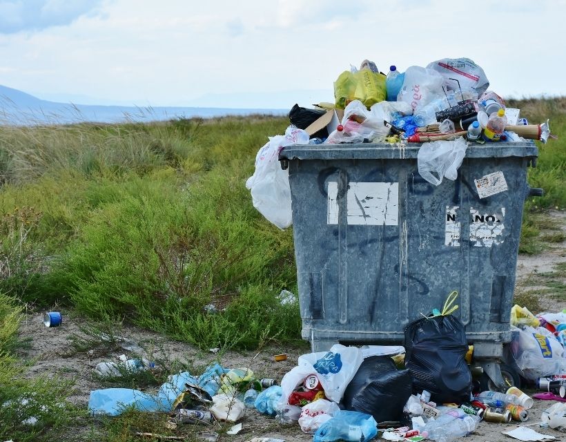 A large waste bucket overflowing in a field. 