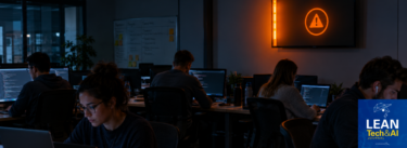 A dark software team room or open office, with a single wall monitor or andon light glowing Orange while the people nearby keep working, heads down. The light is plainly visible and plainly unanswered.